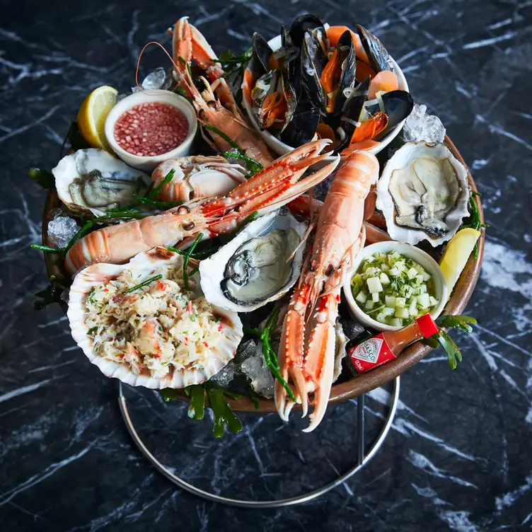 An ice-filled seafood tower with langoustines, mussels, oysters, a crab-stuffed scallop, lemon wedges, and dipping sauces